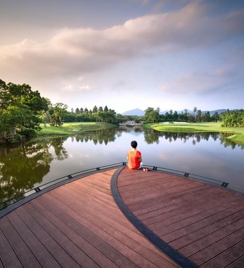 Person meditating peacefully outdoors near a calm lake at sunrise.
